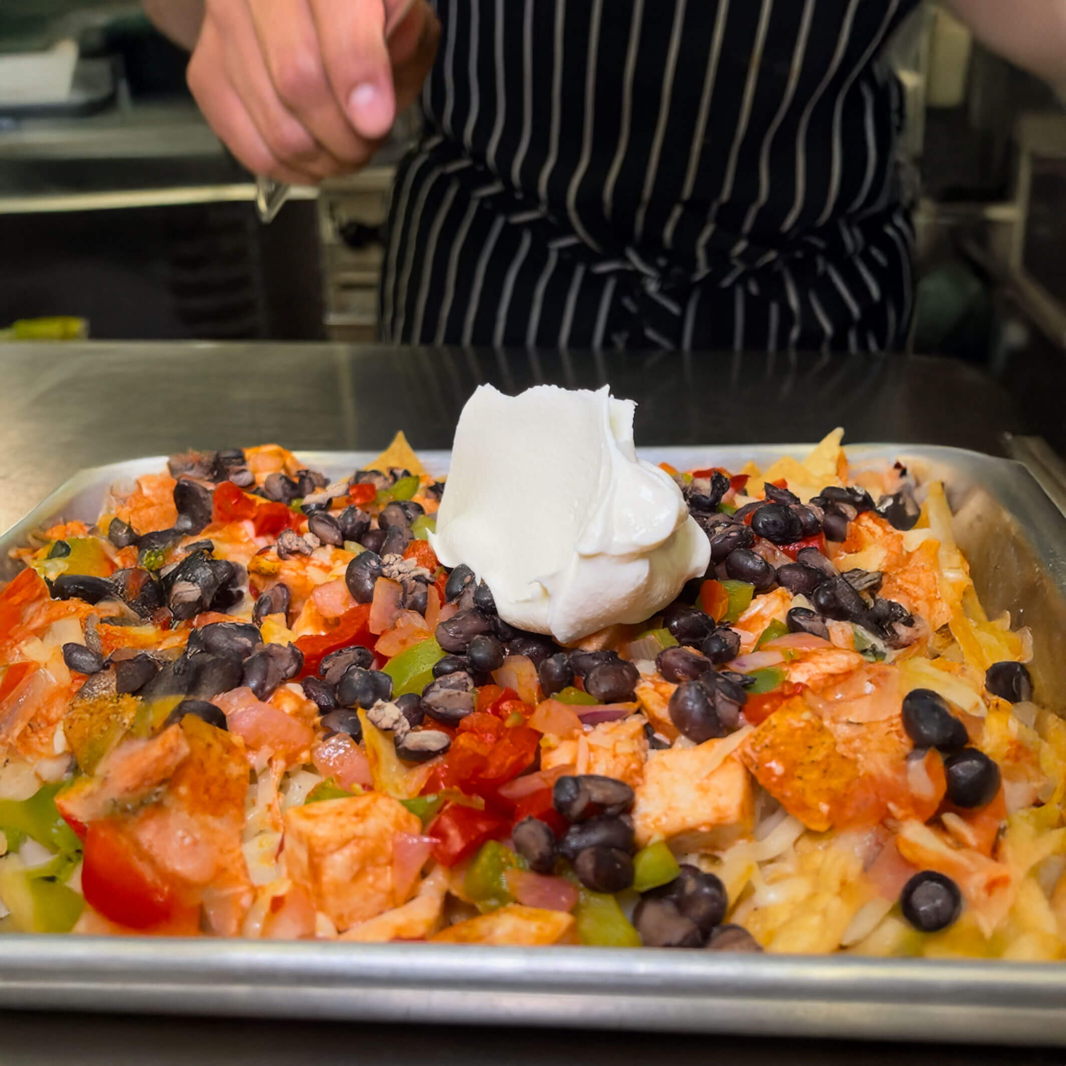 Skillet of buffalo chicken nachos topped with melted cheese, beans, and fresh tomato