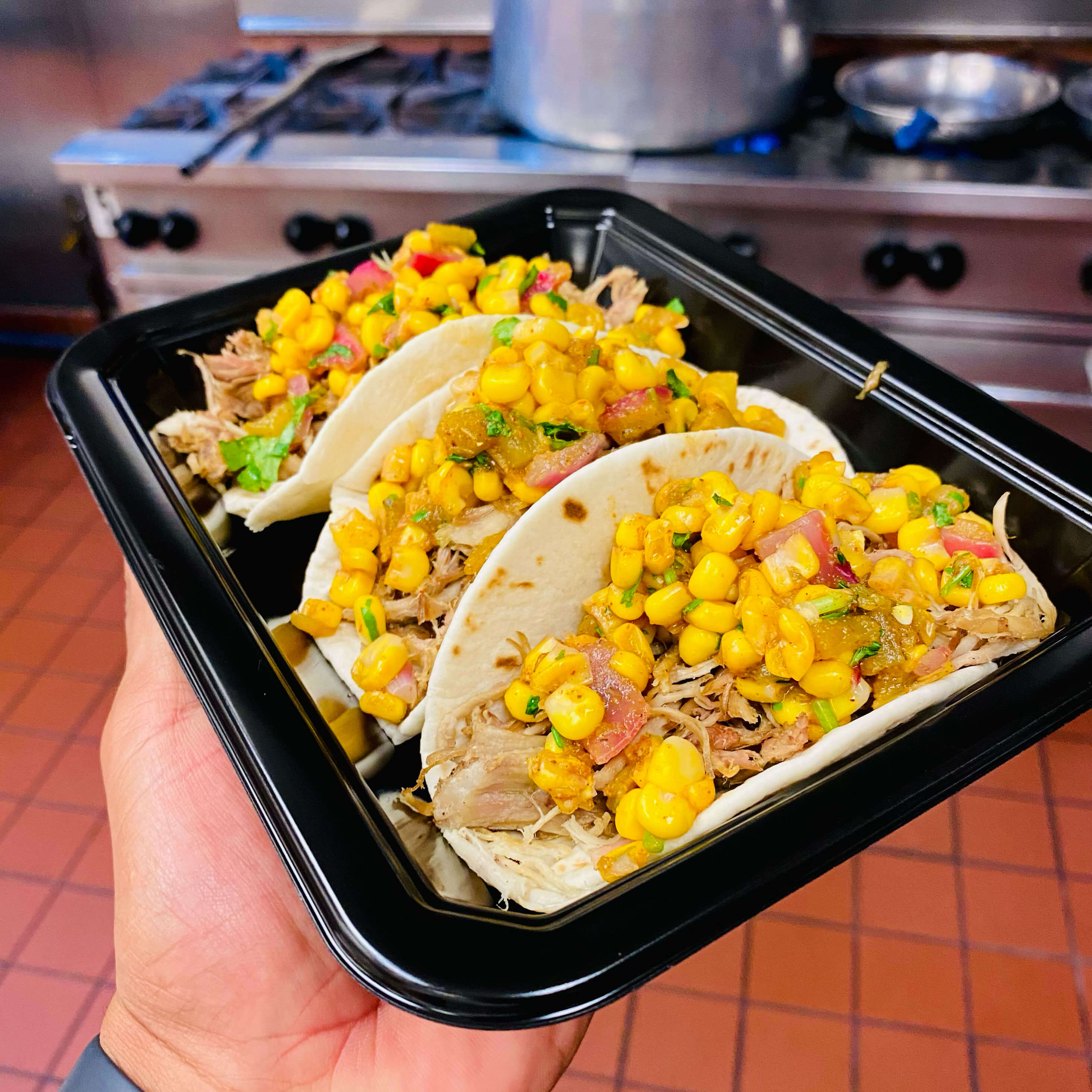Plate of three BBQ pulled‑pork street tacos with cilantro and lime wedges